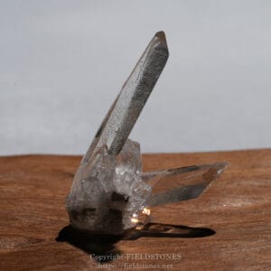 Clear quartz crystal cluster with two long, sharp prism points resting on a wooden surface.