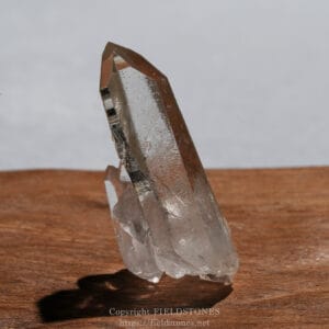 Translucent quartz crystal cluster with a tall, pointed main crystal on a wooden surface.