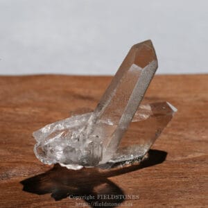 Two clear quartz crystals resting on a wooden surface, lit by natural light.