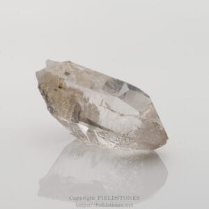 Raw clear quartz crystal with natural facets resting on a white reflective surface