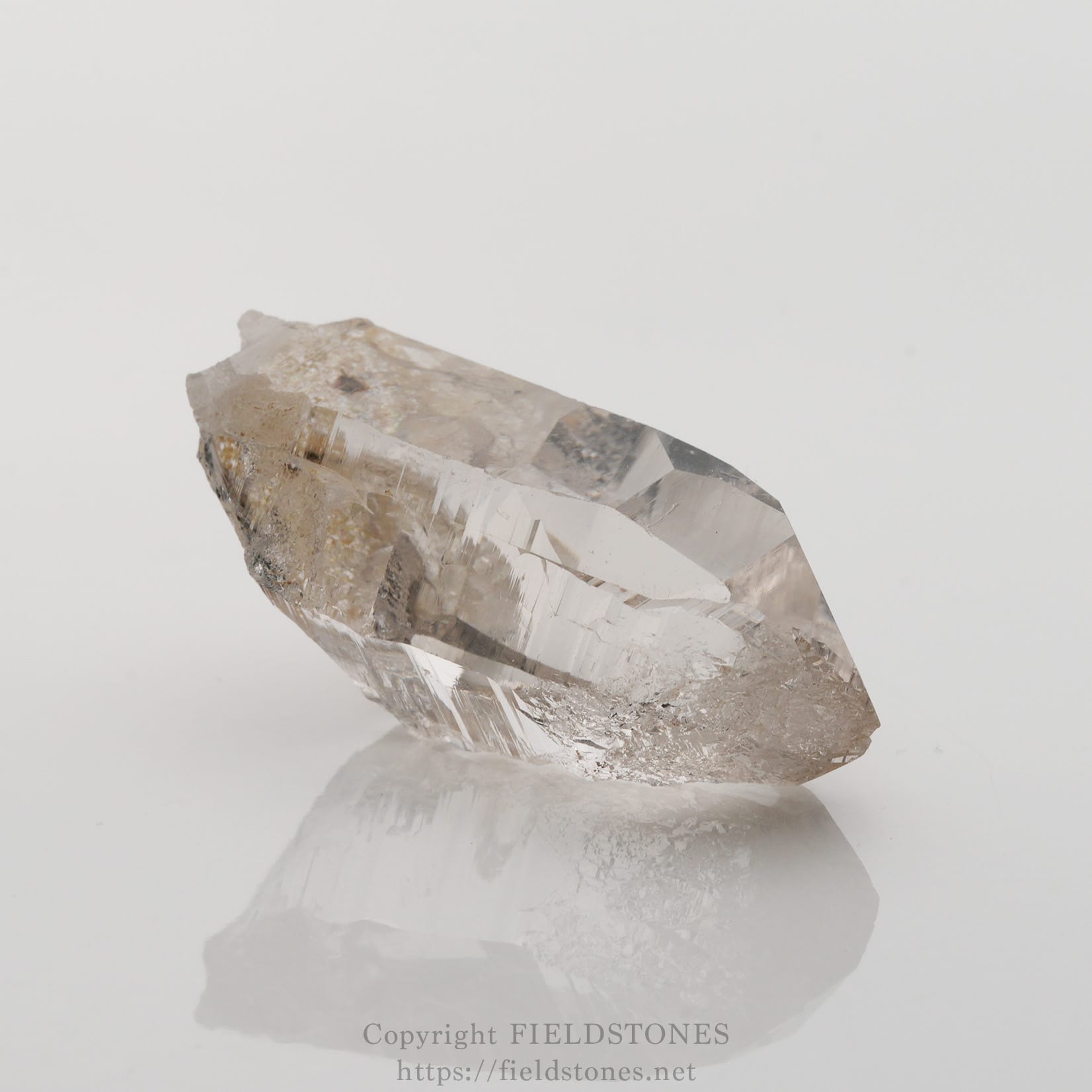 6501-1 - FieldStones Raw clear quartz crystal with natural facets resting on a white reflective surface