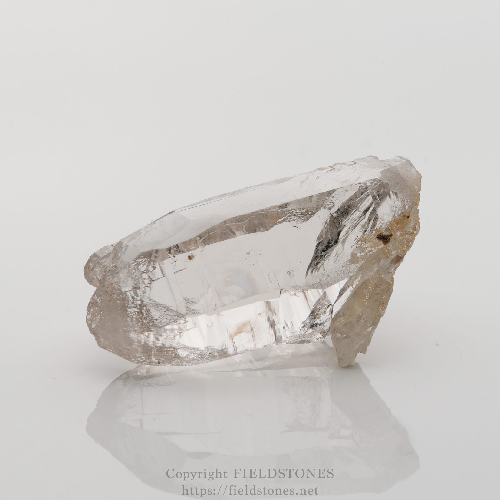 6501-2 - FieldStones Clear quartz crystal with jagged facets resting on a white reflective surface.