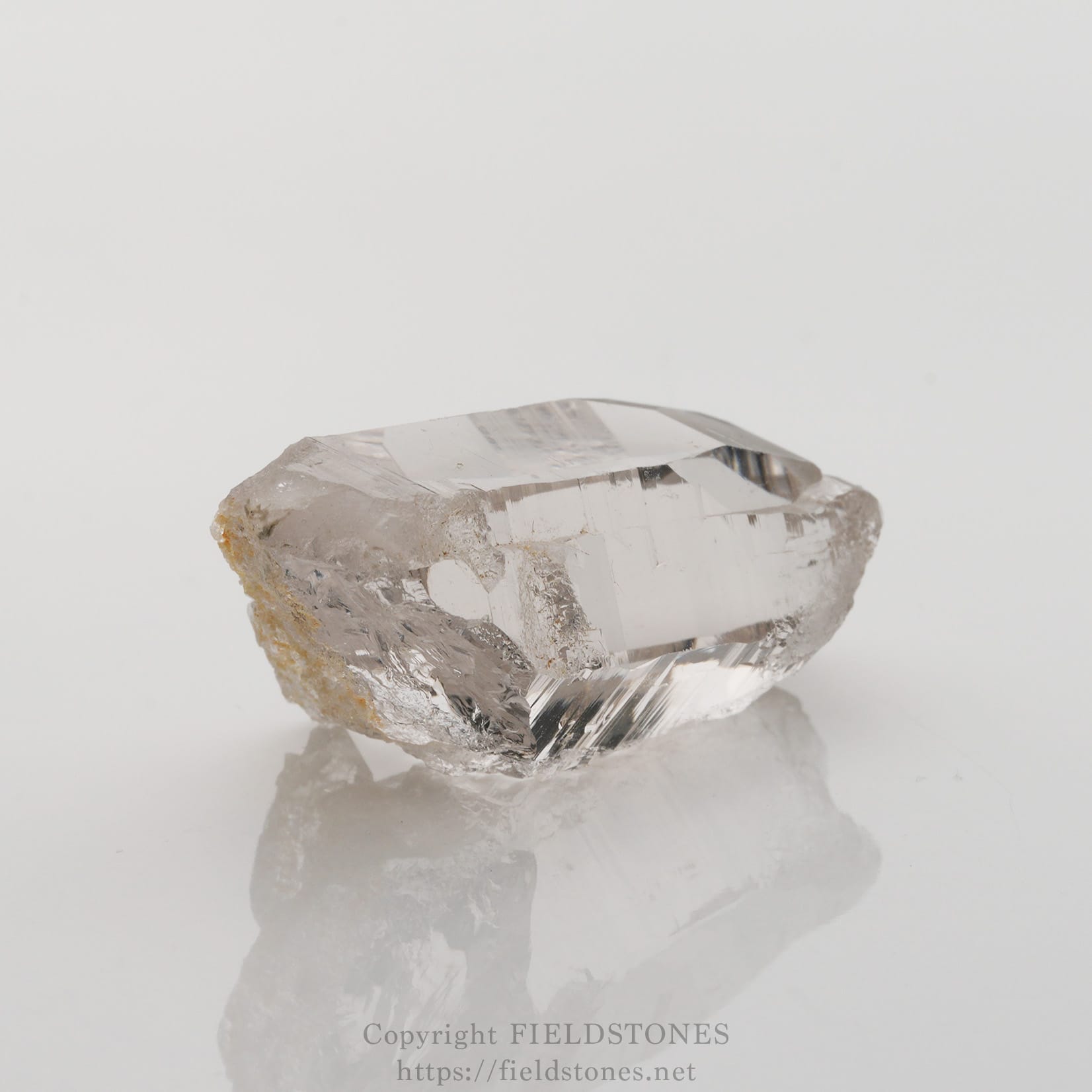 6501-4 - FieldStones Clear quartz crystal on a glossy surface, showing sharp facets and a translucent body.