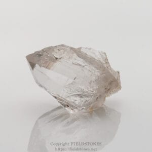 Clear quartz crystal with sharp facets resting on a reflective white surface