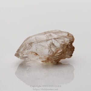 Clear quartz crystal chunk with a brown, earthy base on a glossy white surface with reflection