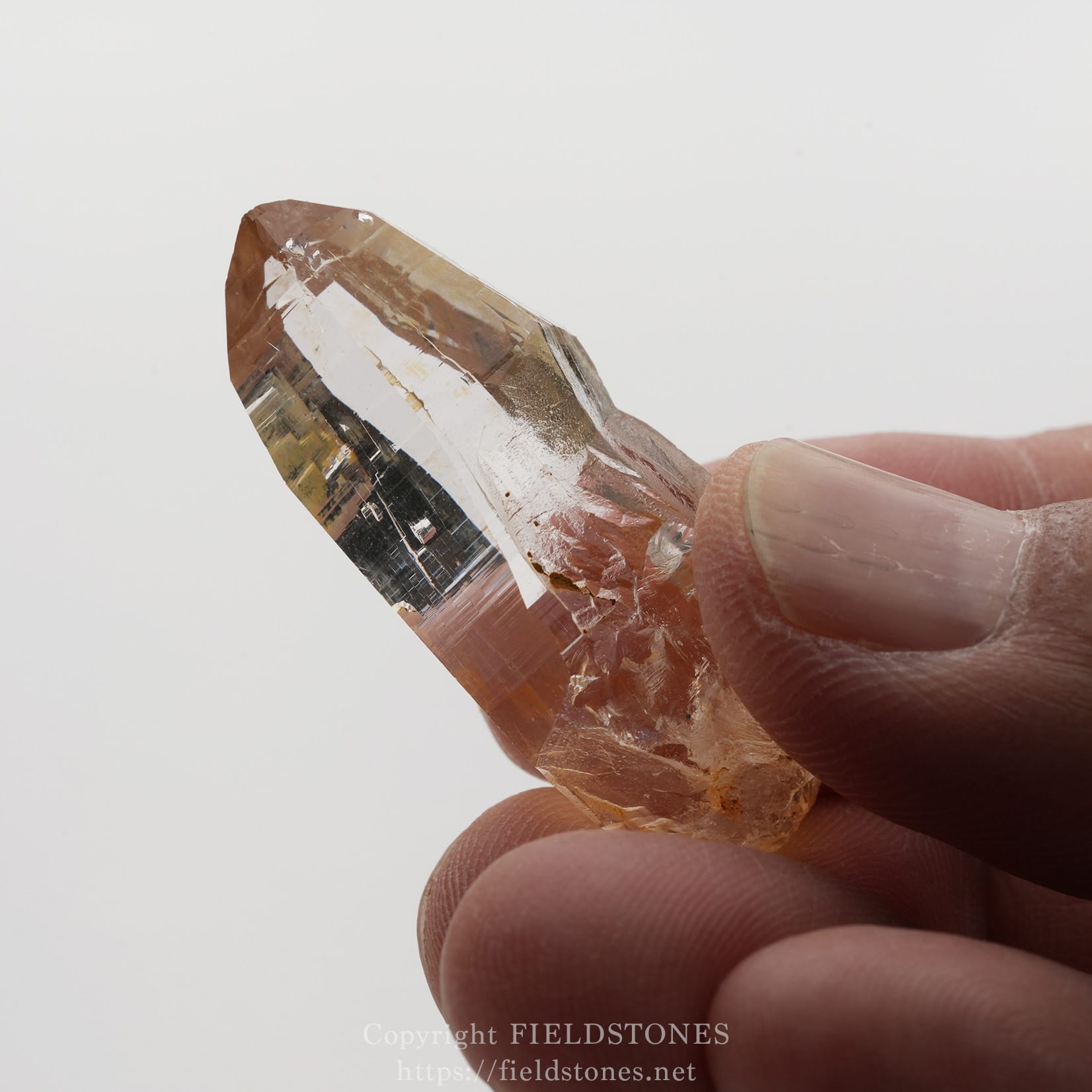 6506-11 - FieldStones Close-up of a peach-colored quartz crystal held between fingertips.