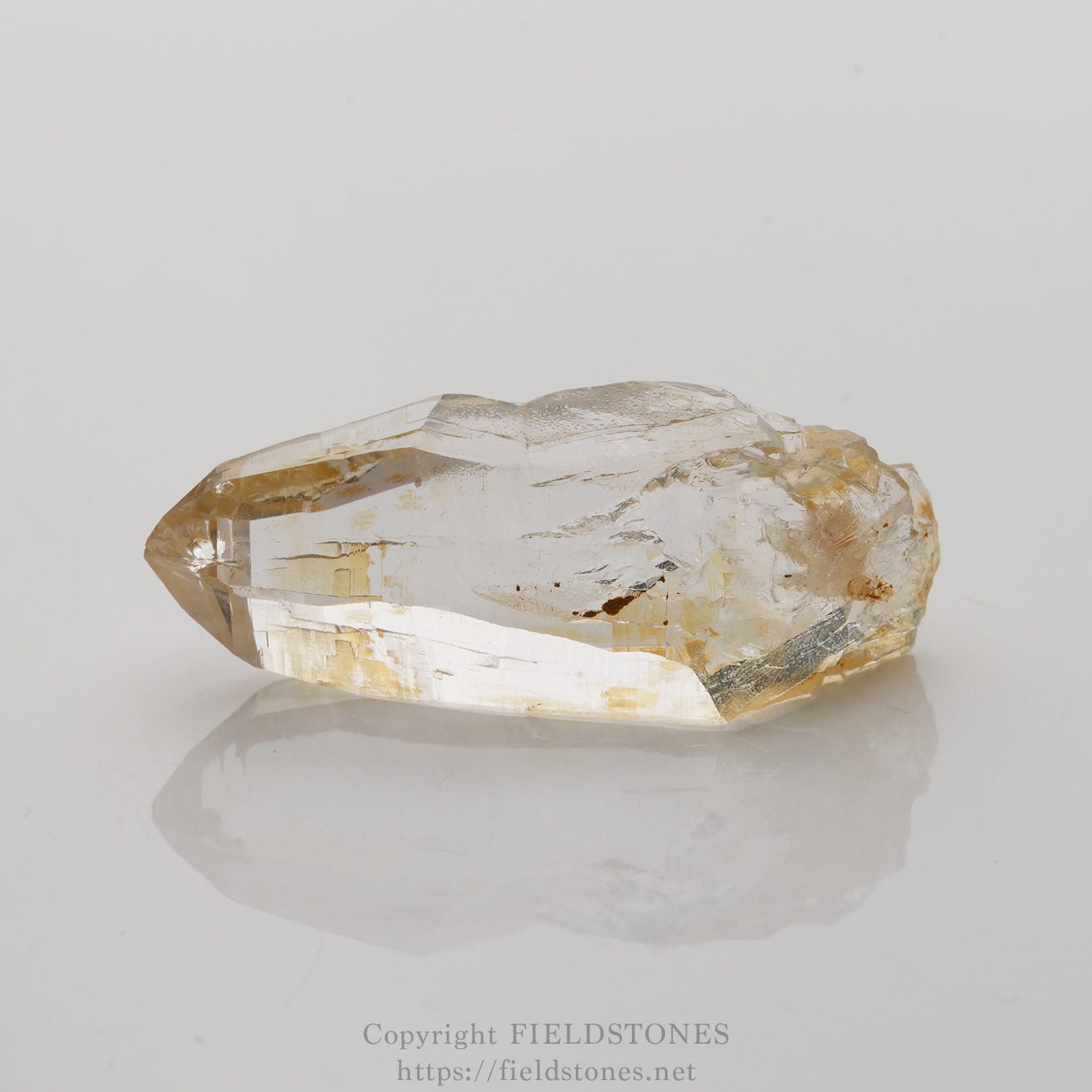 6506-6 - FieldStones Clear quartz crystal point resting on a white surface, showing sharp facets and natural clarity.
