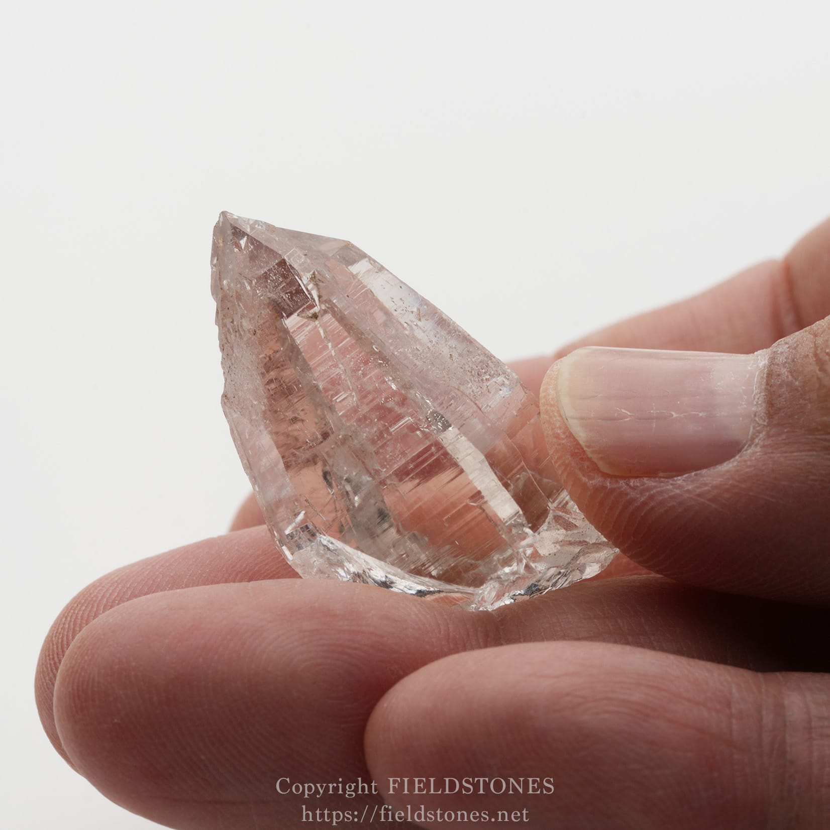 6509-12 - FieldStones Pink quartz crystal held between a thumb and finger, showing sharp, faceted faces.