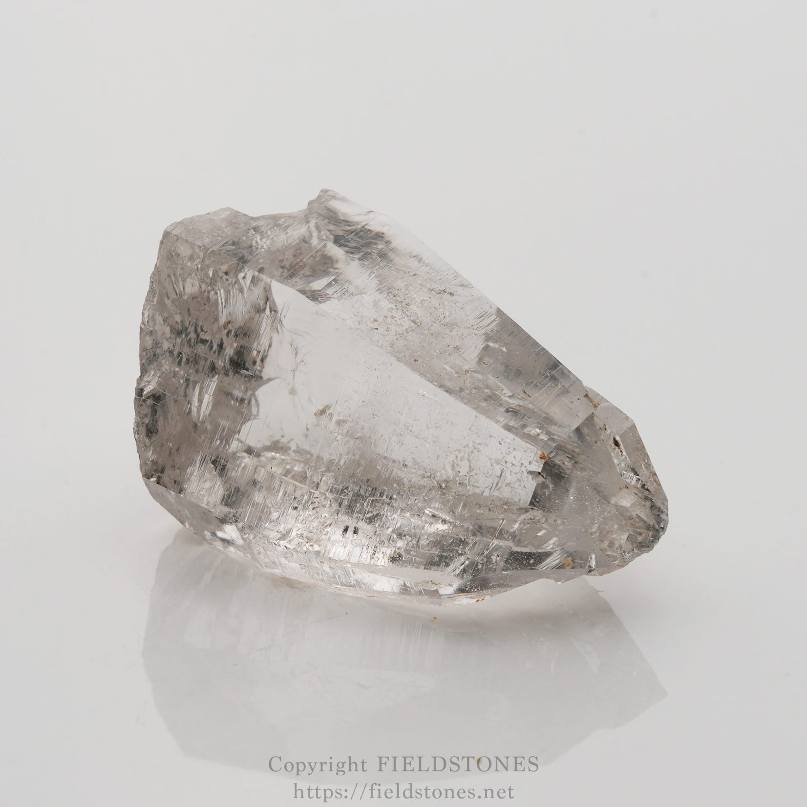 6509-4 - FieldStones Clear quartz crystal on a white surface, showing its translucent, faceted structure and natural imperfections.