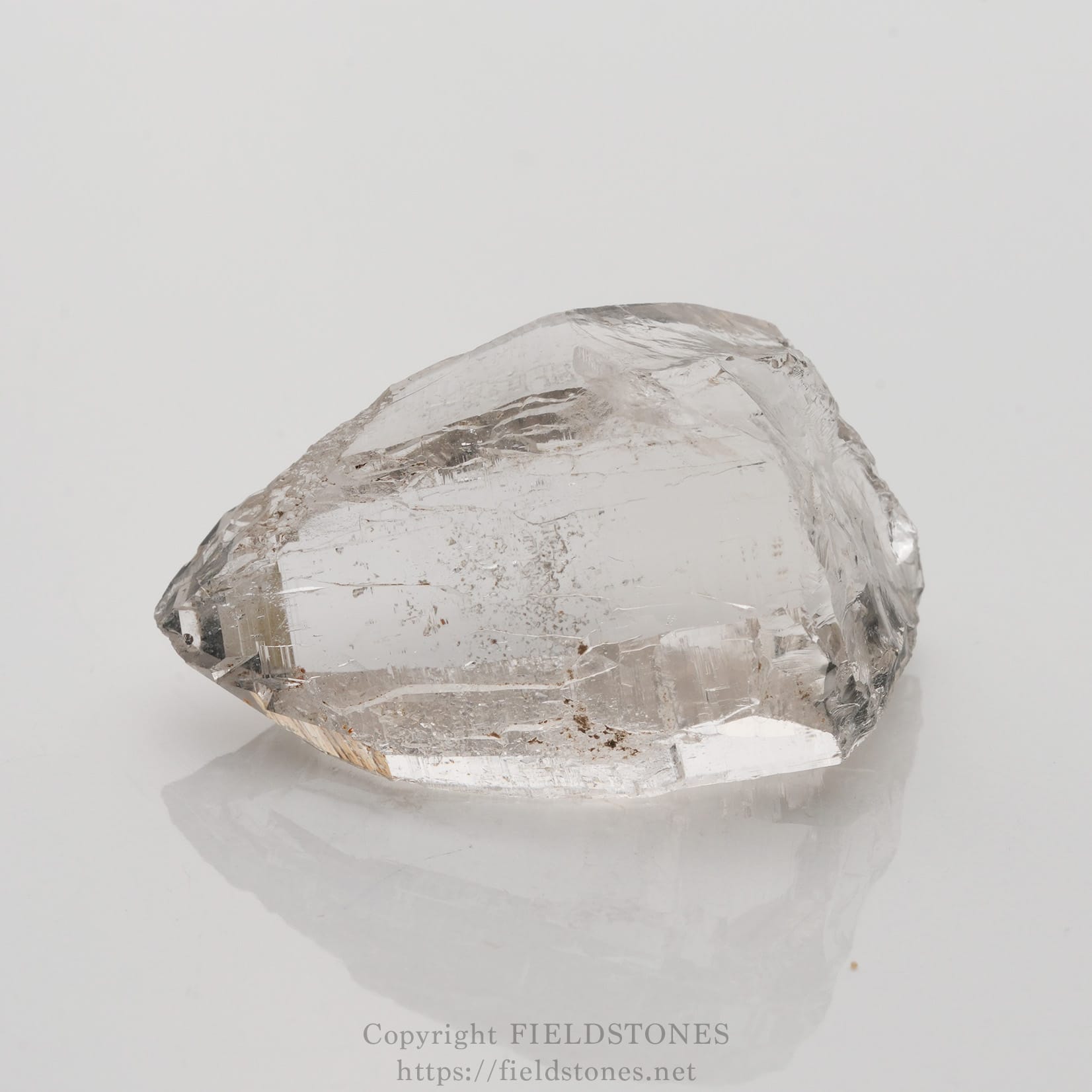 6509-6 - FieldStones Clear quartz crystal on a white background, showing a pale, transparent, faceted stone with natural inclusions.
