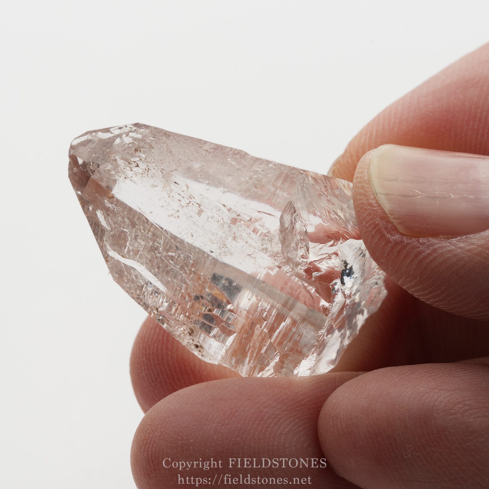 6509-9 - FieldStones Close-up of a translucent pink quartz crystal being pinched between fingertips.