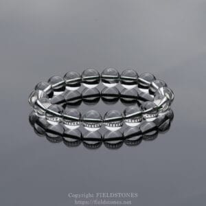 Clear glass bead bracelet arranged in a circular loop on a glossy reflective surface, showcasing smooth, transparent beads.
