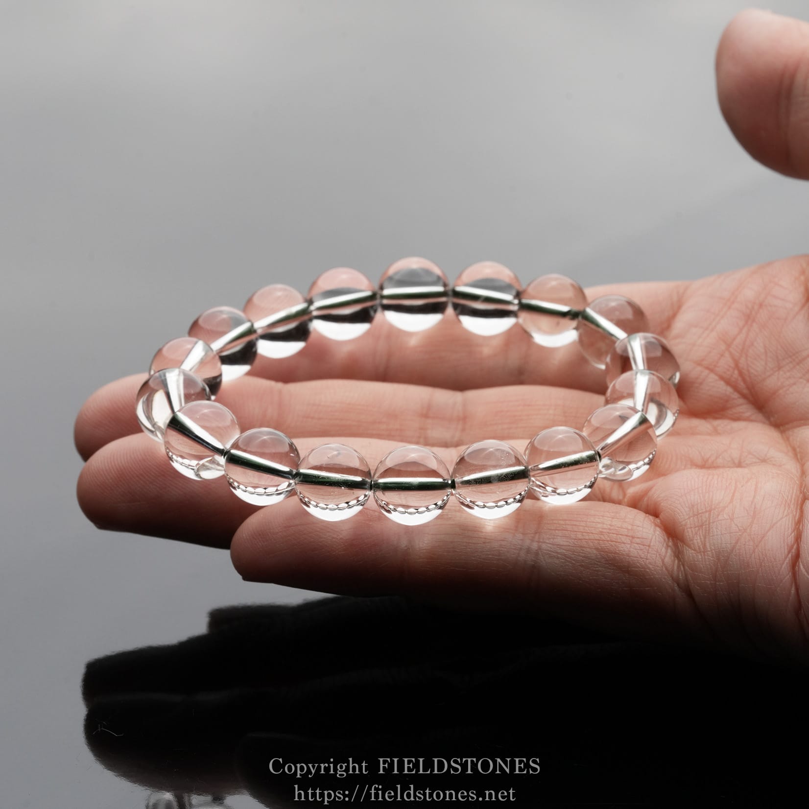 6512-12 - FieldStones Clear glass bead bracelet held on a person's open palm, featuring evenly sized transparent spheres threaded on a string.