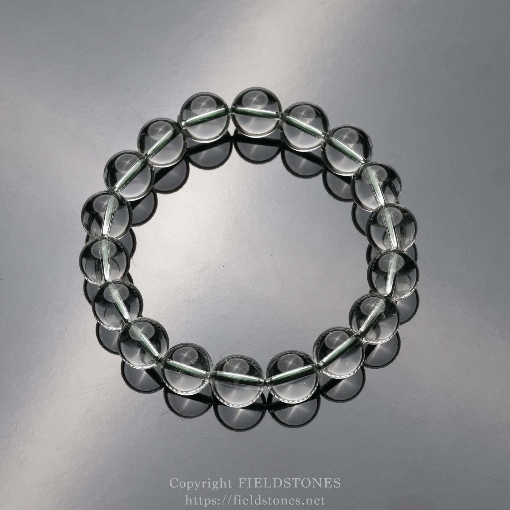 6512-4 - FieldStones Circular bracelet made of translucent glass beads on a reflective surface, with pale green spacer threads visible between beads (jewelry image).