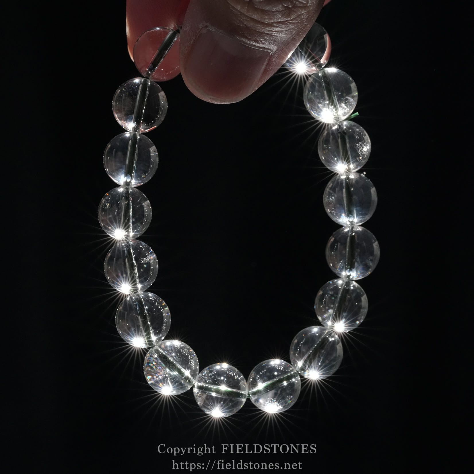 6512-5 - FieldStones Clear glass bead bracelet held against a dark background, each bead sparkling with light reflections.