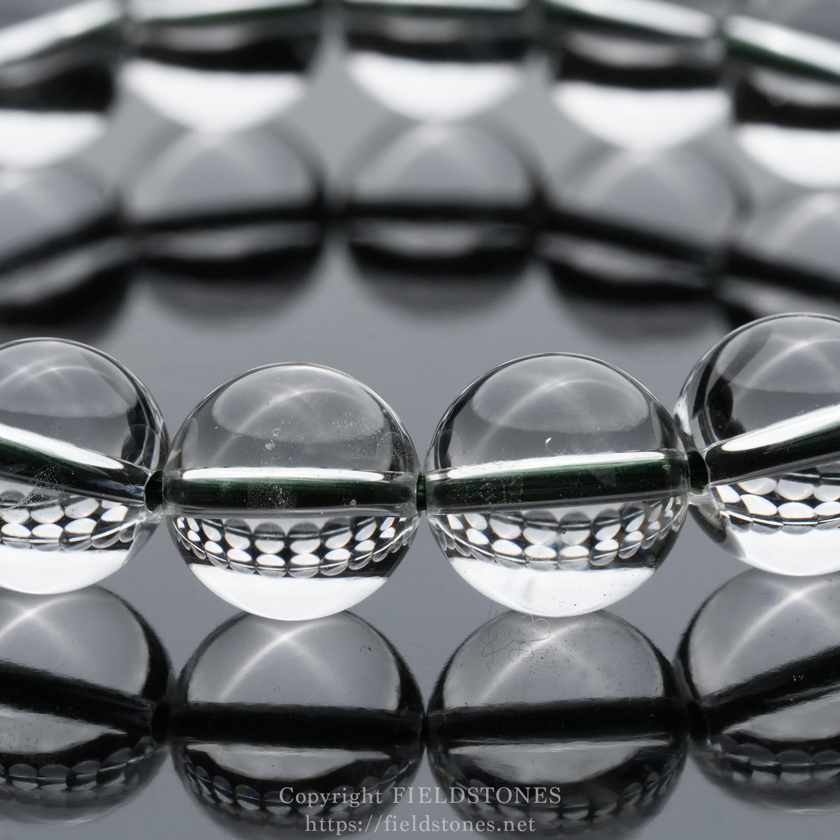 6512-7 - FieldStones Row of clear glass marbles on a reflective black surface, creating mirrored reflections in the water-like finish.