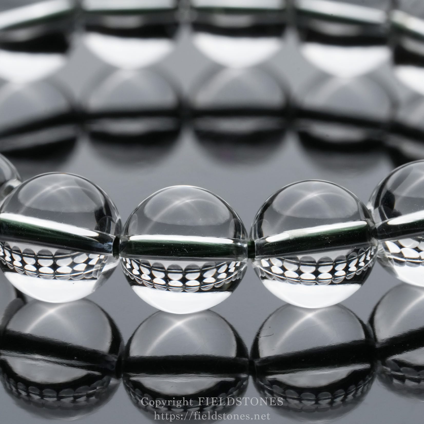 6512-8 - FieldStones Close-up of a row of clear glass beads lying on a glossy, reflective surface with bright reflections nearby.