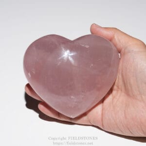 Pink rose quartz heart cradled in a palm, shown in close-up.