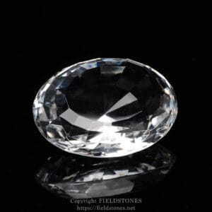 Oval-cut clear diamond resting on a black reflective surface, showing bright faceted facets and subtle reflections.