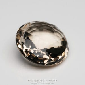 Oval faceted gemstone with champagne-beige tone on a light background; glossy, reflective facets.