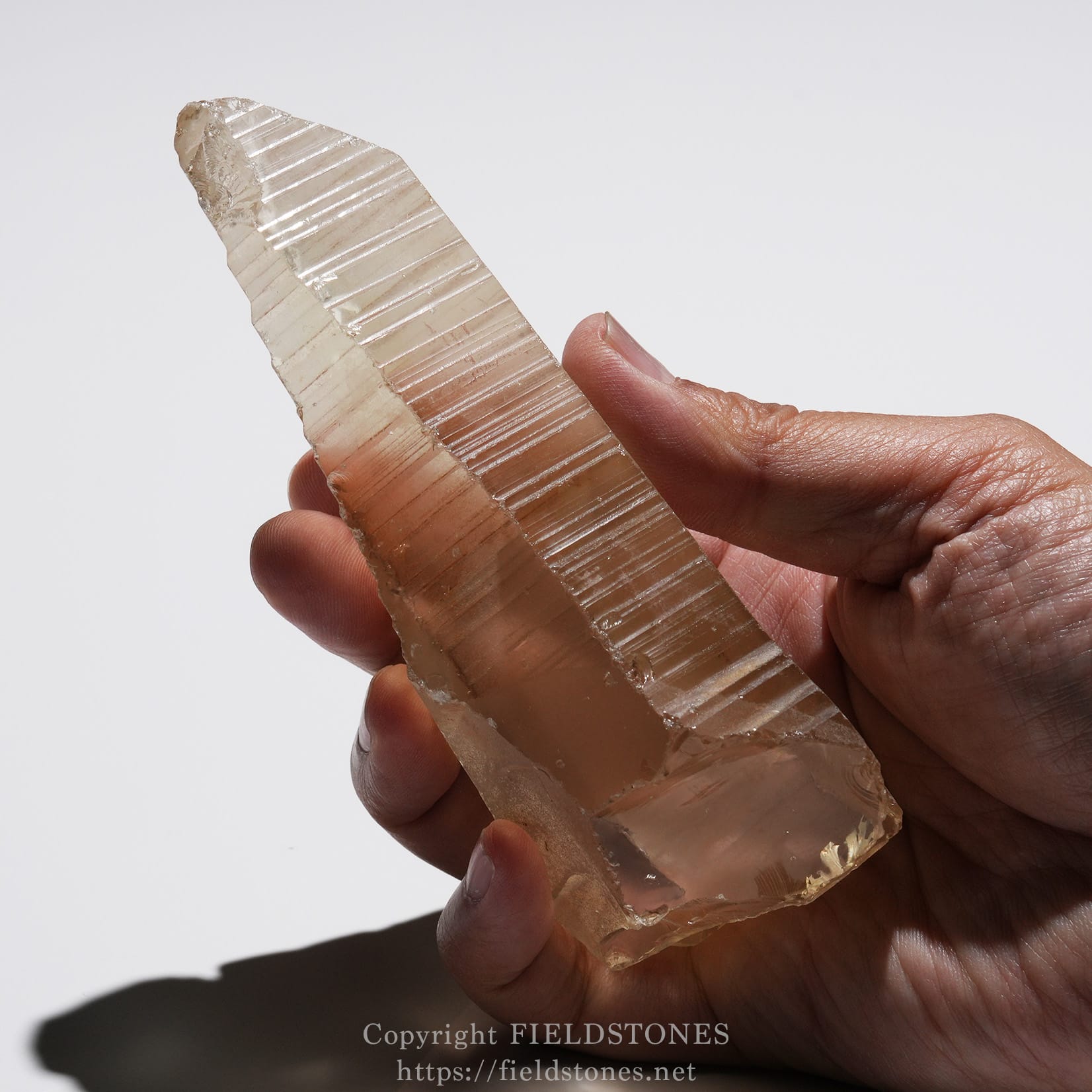 6524-13 - FieldStones Rose quartz crystal held in a hand, showing a pale pink, translucent tabular prism.