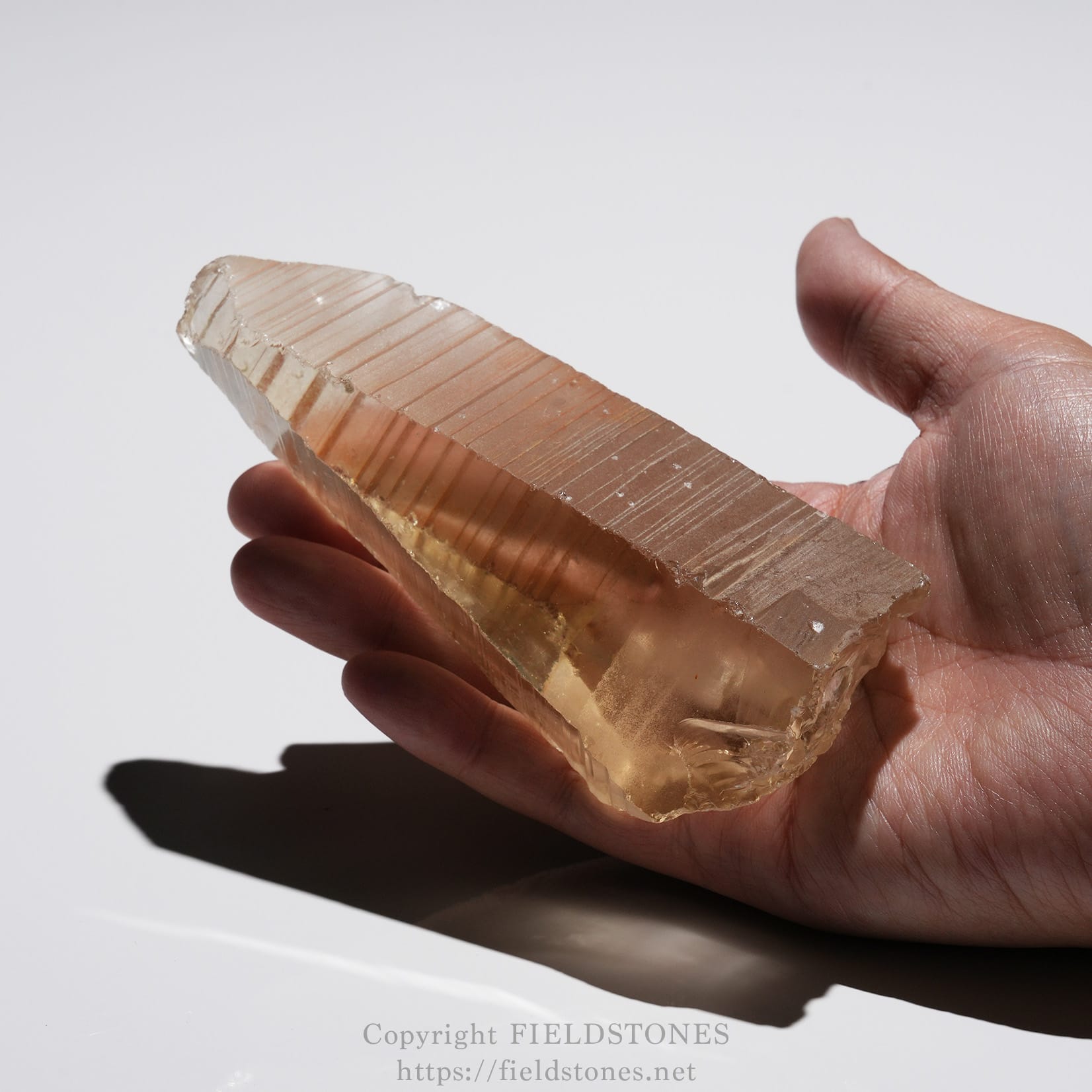 6524-15 - FieldStones Palm-sized clear quartz crystal with horizontal striations held in a hand, showcasing its natural facets and pale pinkish tint.