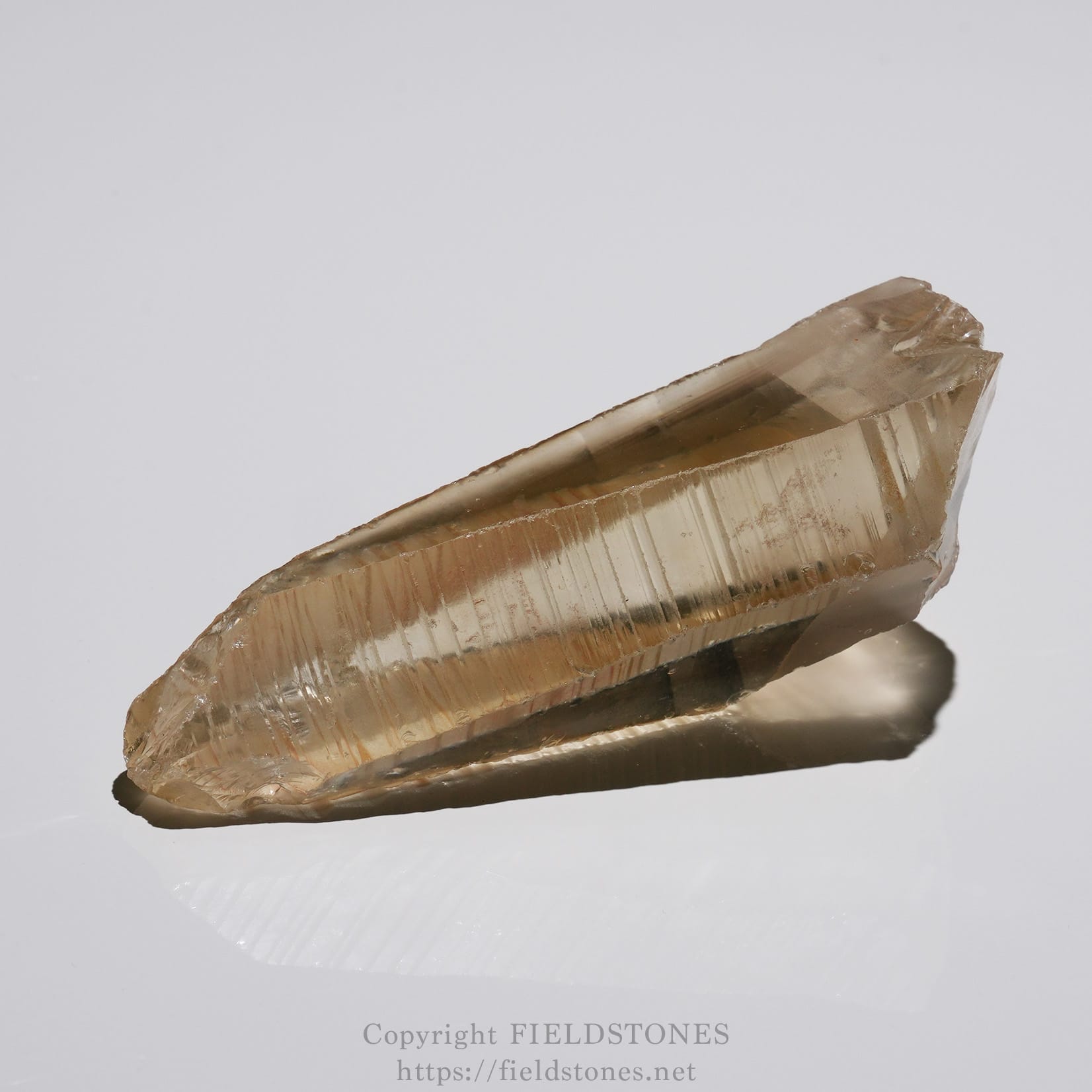 6524-2 - FieldStones Smoky quartz crystal with long hexagonal facets resting on a reflective white surface.