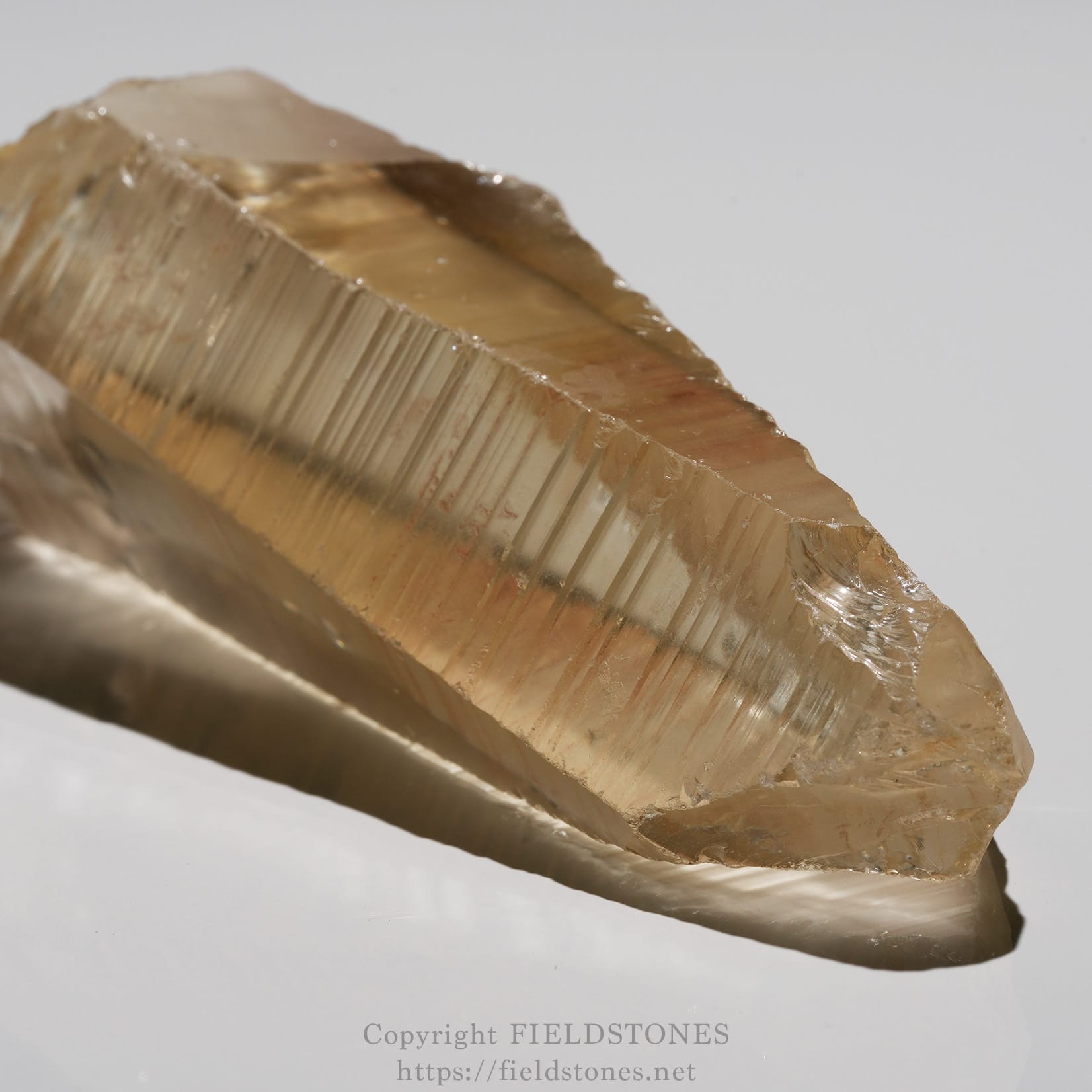 6524-4 - FieldStones Raw, beige crystal specimen with prominent parallel striations and a sharp terminated edge on a white surface.