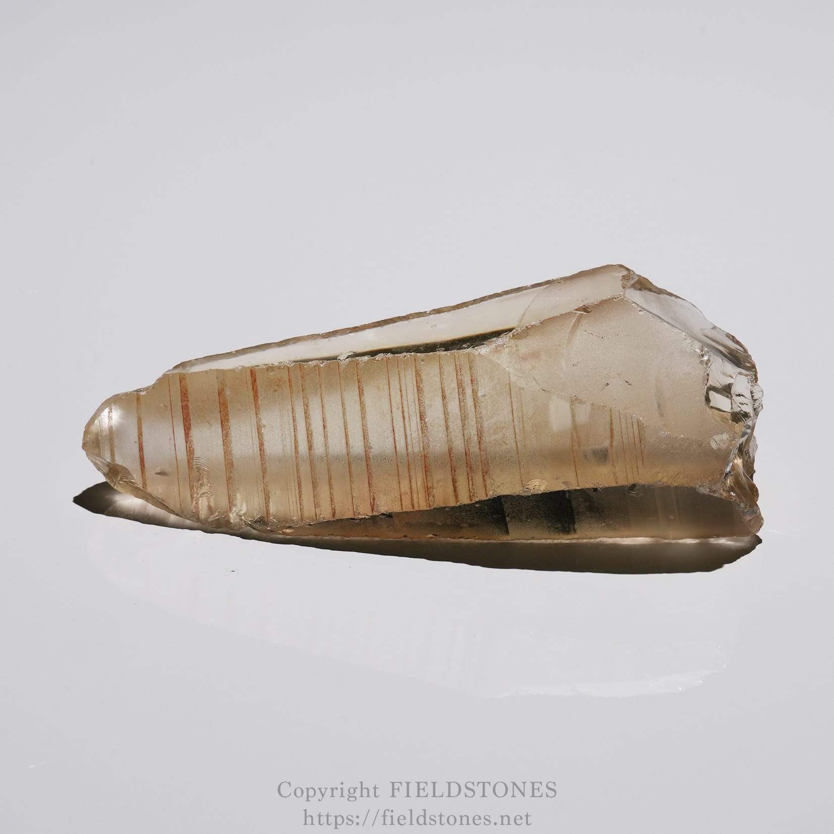 6524-8 - FieldStones Translucent quartz crystal with vertical striations resting on a reflective surface.