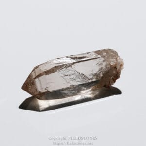Brownish quartz crystal with sharp facets resting on a white surface, casting a shadow to the left.