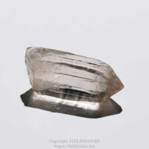 Translucent quartz crystal resting on a reflective white surface with visible facets.