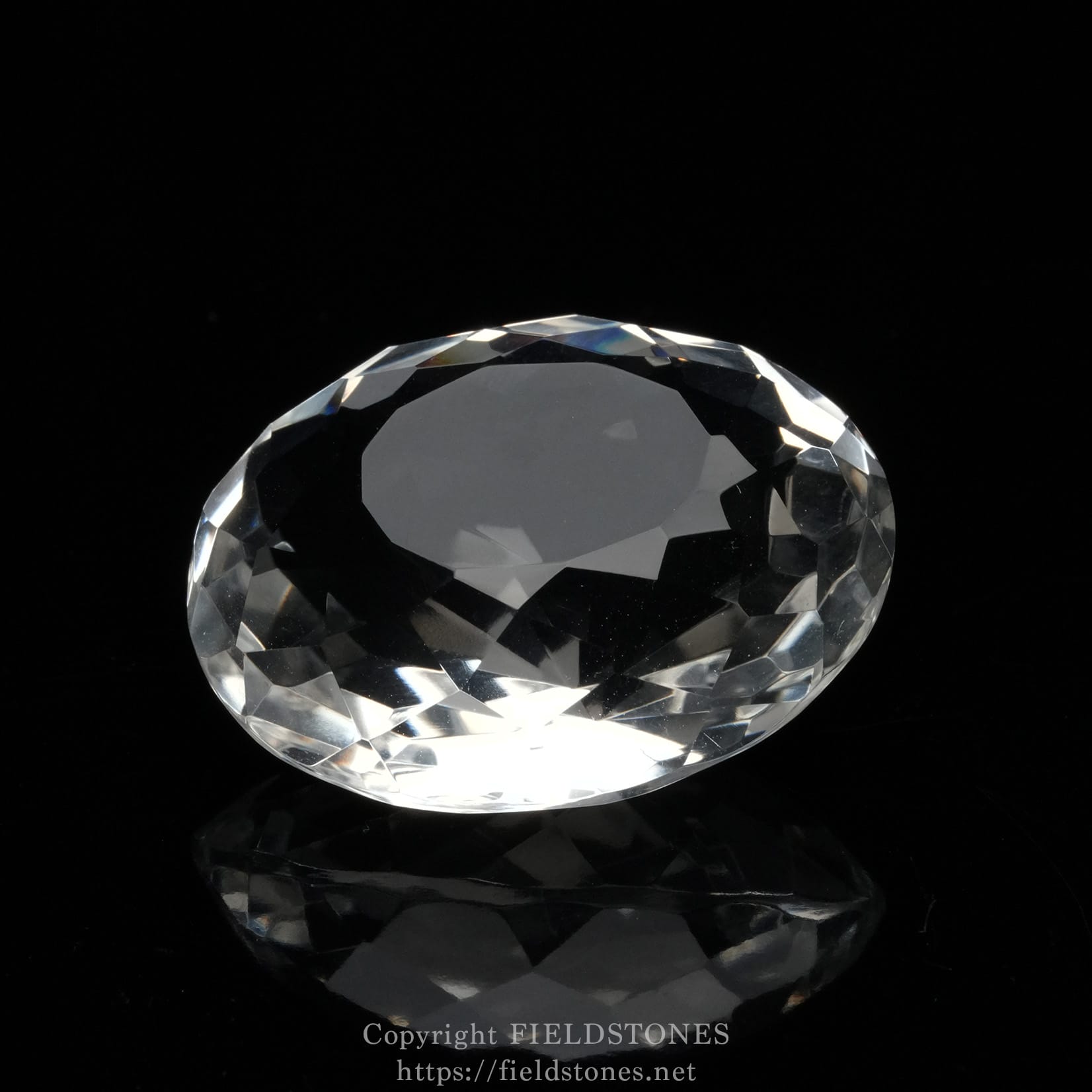 6537-10 - FieldStones Close-up of a clear, faceted diamond resting on a black reflective surface with soft highlights.