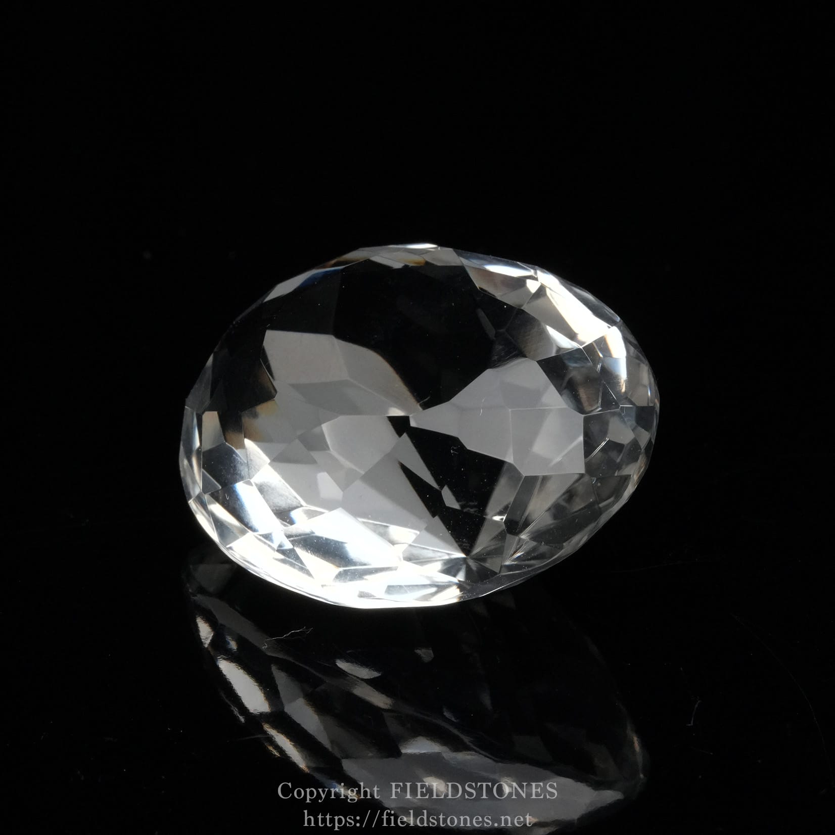 6537-11 - FieldStones Close-up of a large faceted crystal diamond resting on a black reflective surface in low light.