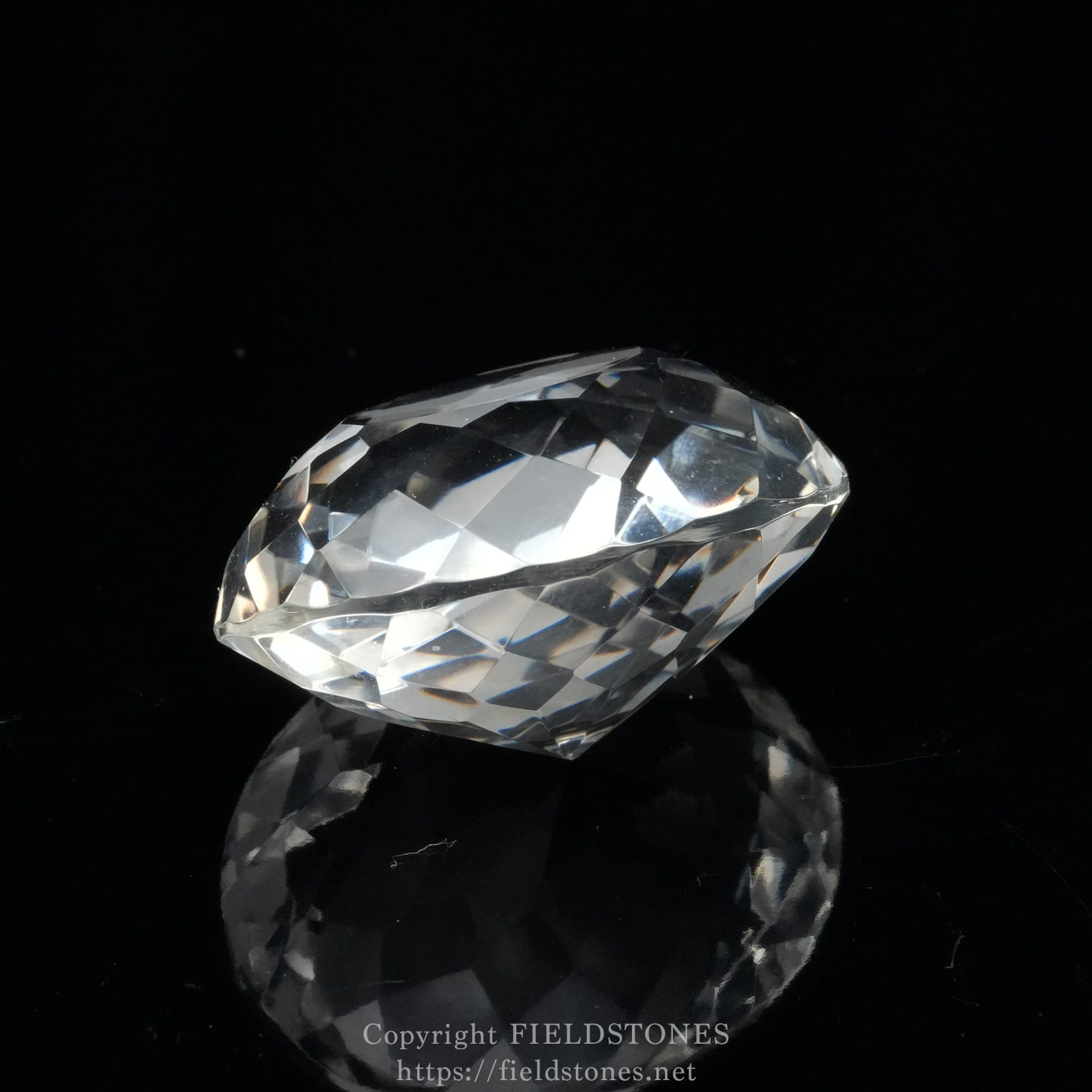 6537-12 - FieldStones Oval-cut diamond resting on a black reflective surface, facets sparkling with light reflections for an elegant look.