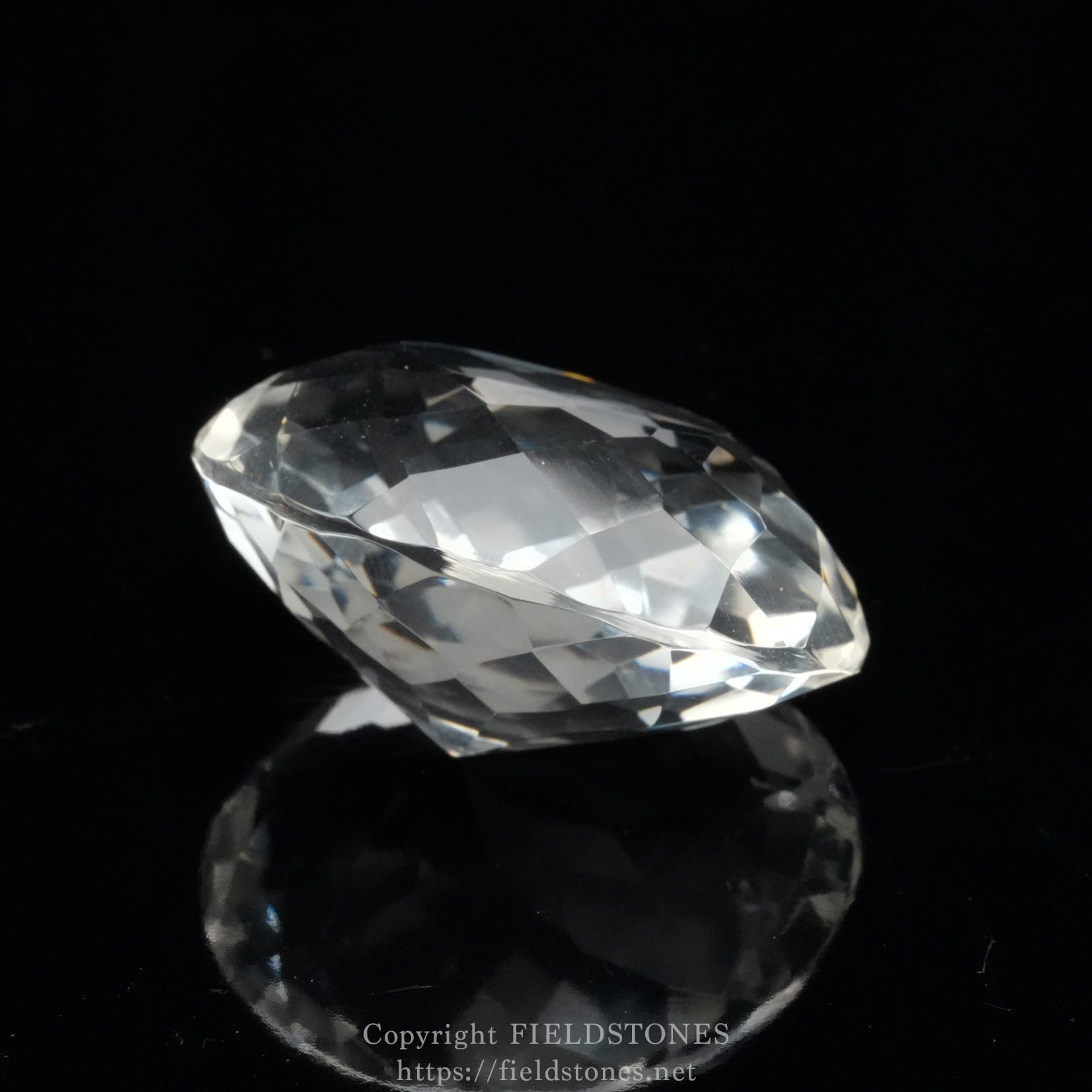 6537-13 - FieldStones Close-up of a faceted clear diamond resting on a black reflective surface, capturing light and sparkle.