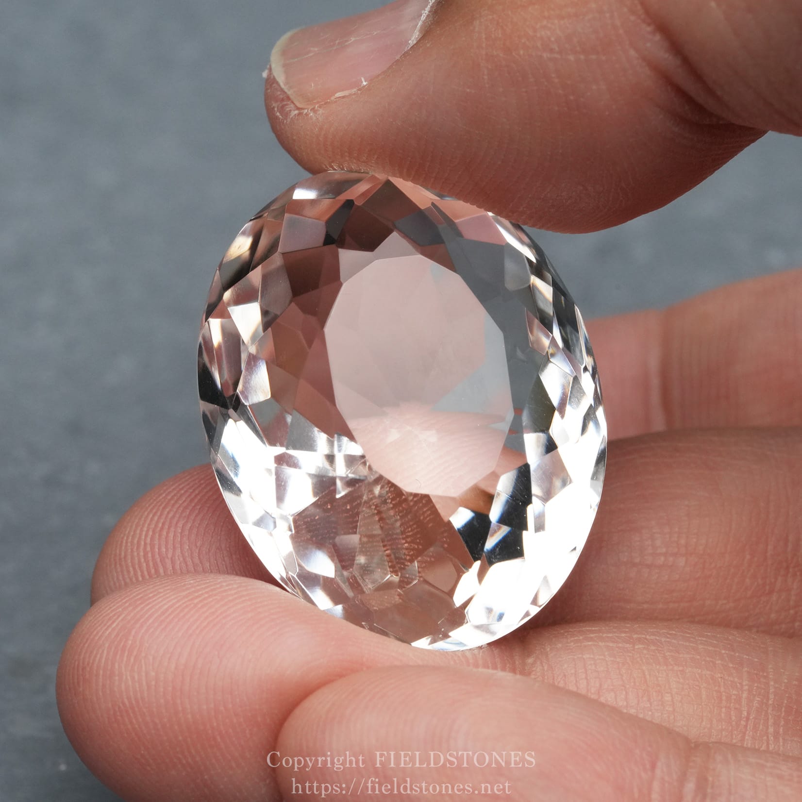6537-5 - FieldStones Close-up of a faceted clear gemstone held between two fingers.
