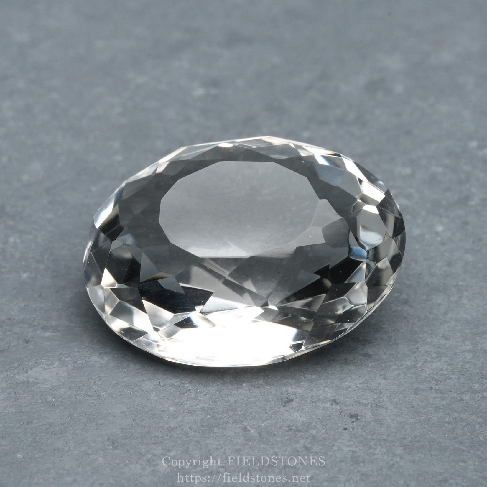 6537-7 - FieldStones Close-up of a large, faceted clear diamond resting on a gray surface.