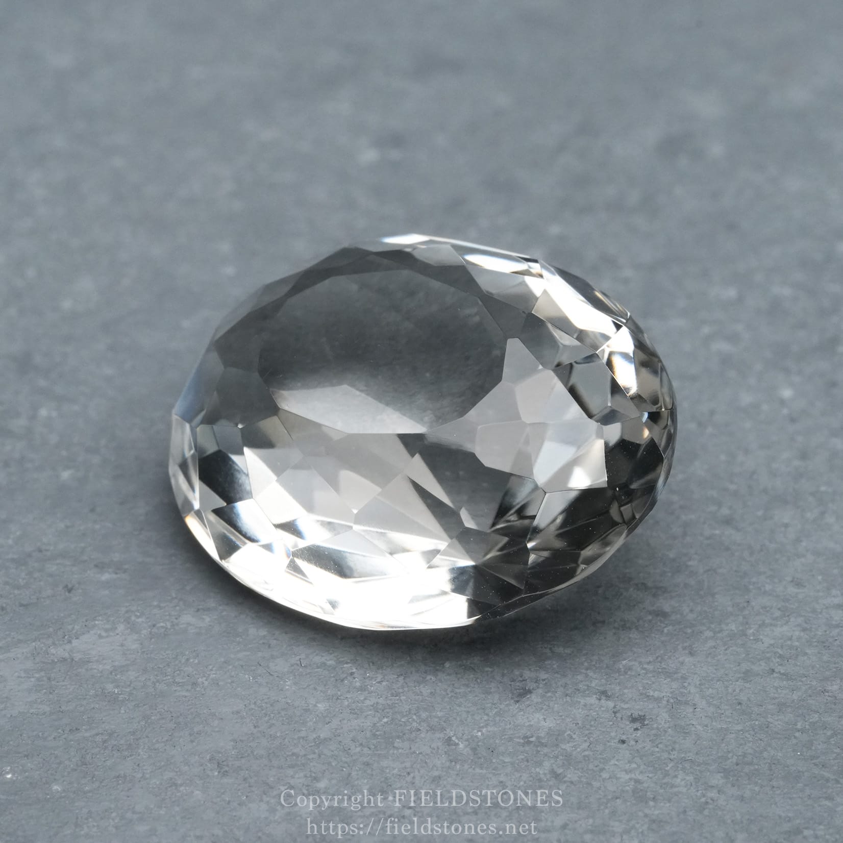 6537-8 - FieldStones Faceted crystal sphere resting on a gray textured surface, reflecting light.