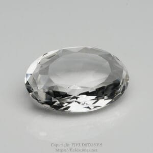 Oval, brilliant-cut diamond resting on a pale gray surface, showing its many facets and reflections.