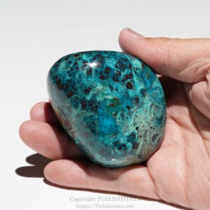 Polished turquoise stone with red matrix held between fingers in a hand