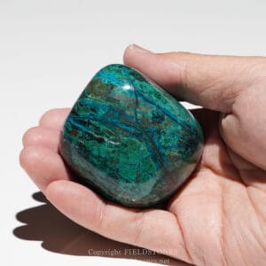 Person holds a polished green-blue gemstone with blue veins between green and teal areas.