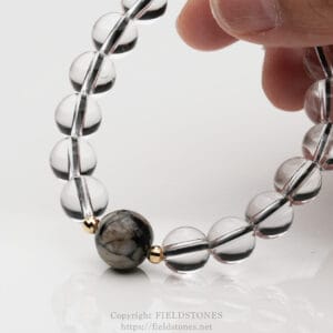 Close-up of a translucent glass bead bracelet being pinched by fingers over a reflective white surface.