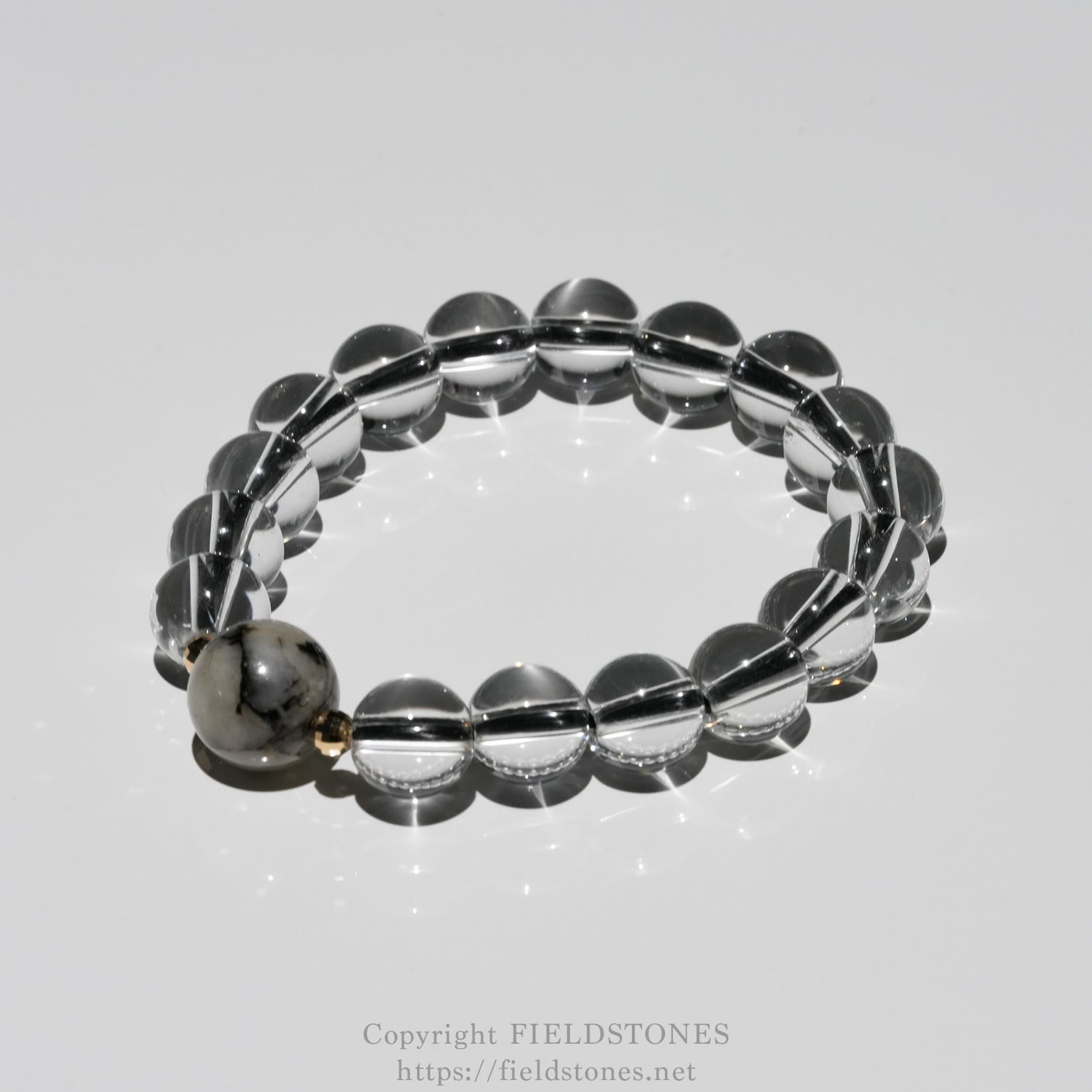 6547-2 - FieldStones Clear glass bead bracelet arranged in a circular shape on a reflective surface.