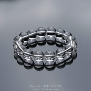 Clear glass bead bracelet arranged in a loop on a reflective surface with a gray gradient background.