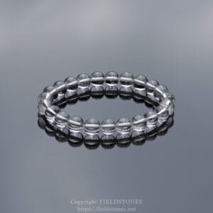Clear beaded bracelet made of translucent glass on a mirrored surface, forming a circle with reflections beneath it.