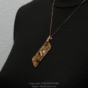 Gold chain necklace with a clear crystal pendant resting on a black fabric surface.