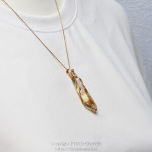 Gold chain necklace with a faceted crystal pendant resting on a white fabric surface.