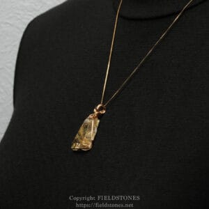 Gold chain necklace with a crystal pendant resting on black fabric background