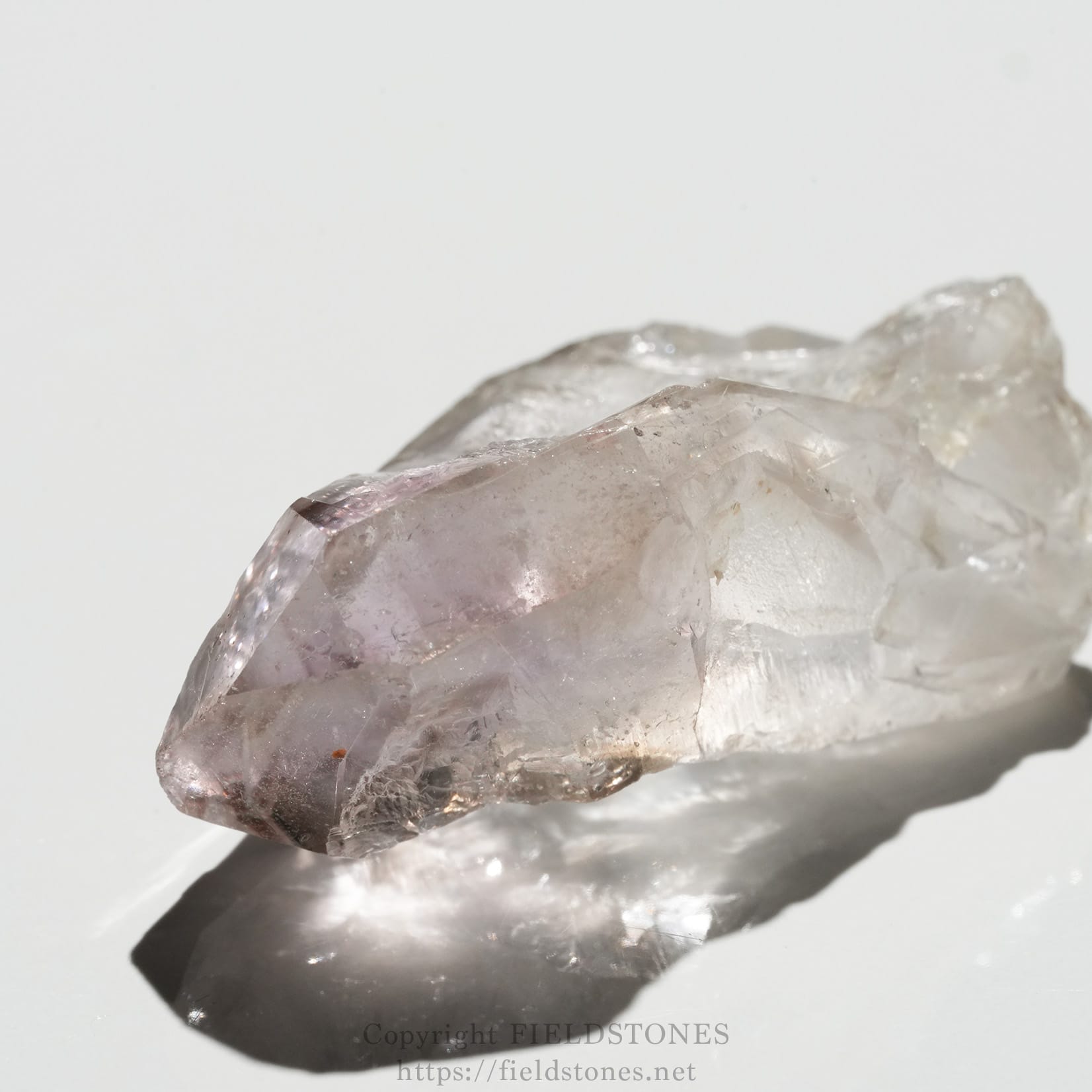 6562-1 - FieldStones Close-up of a pale lavender amethyst crystal cluster with sharp facets on a white surface, showing translucence and natural growth patterns.