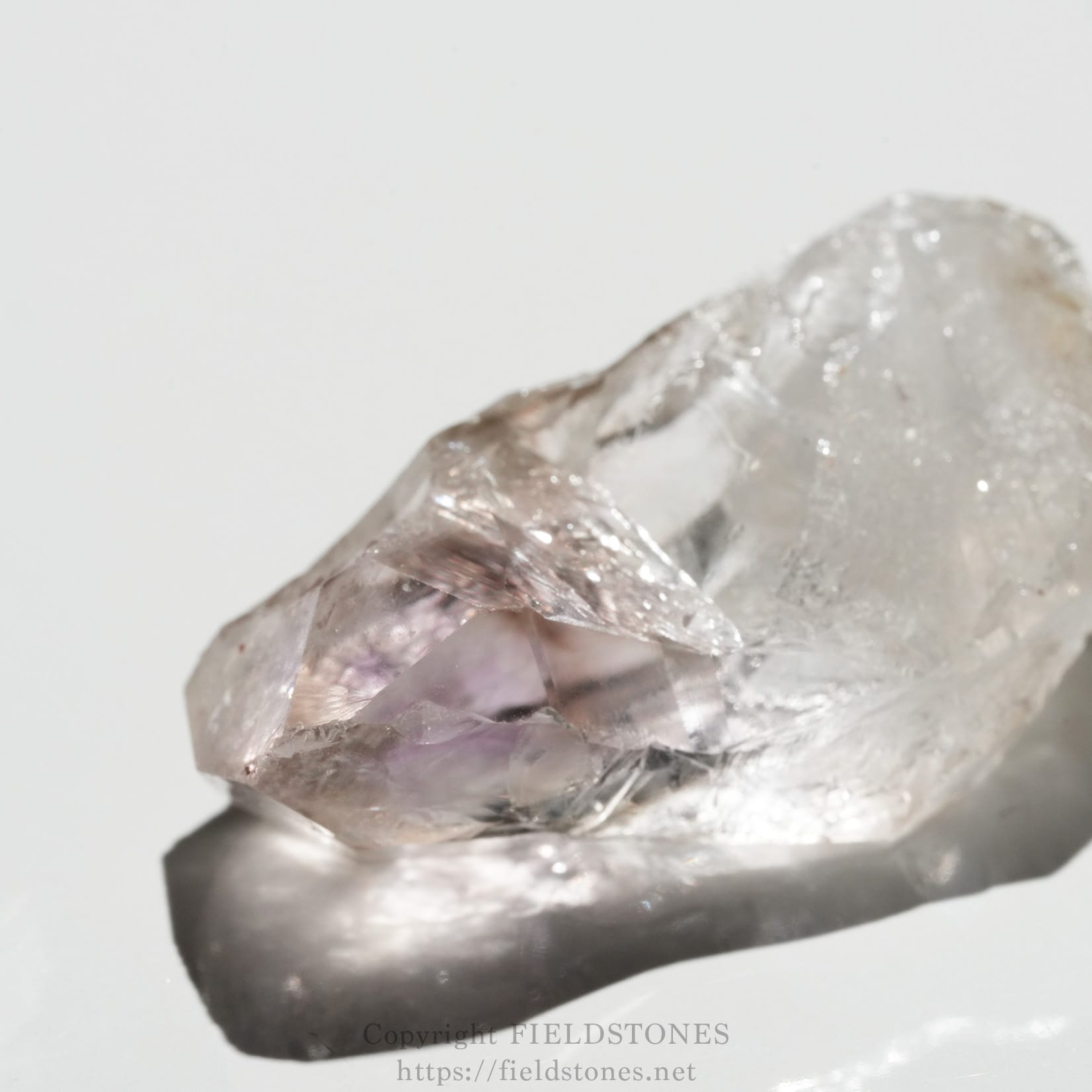 6562-3 - FieldStones Close-up of a lavender quartz (amethyst) crystal with rough, faceted surfaces on a light background, highlighting its translucency.